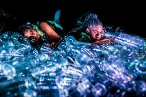 Two people in mermaid costumes surrounded by plastic bottles.